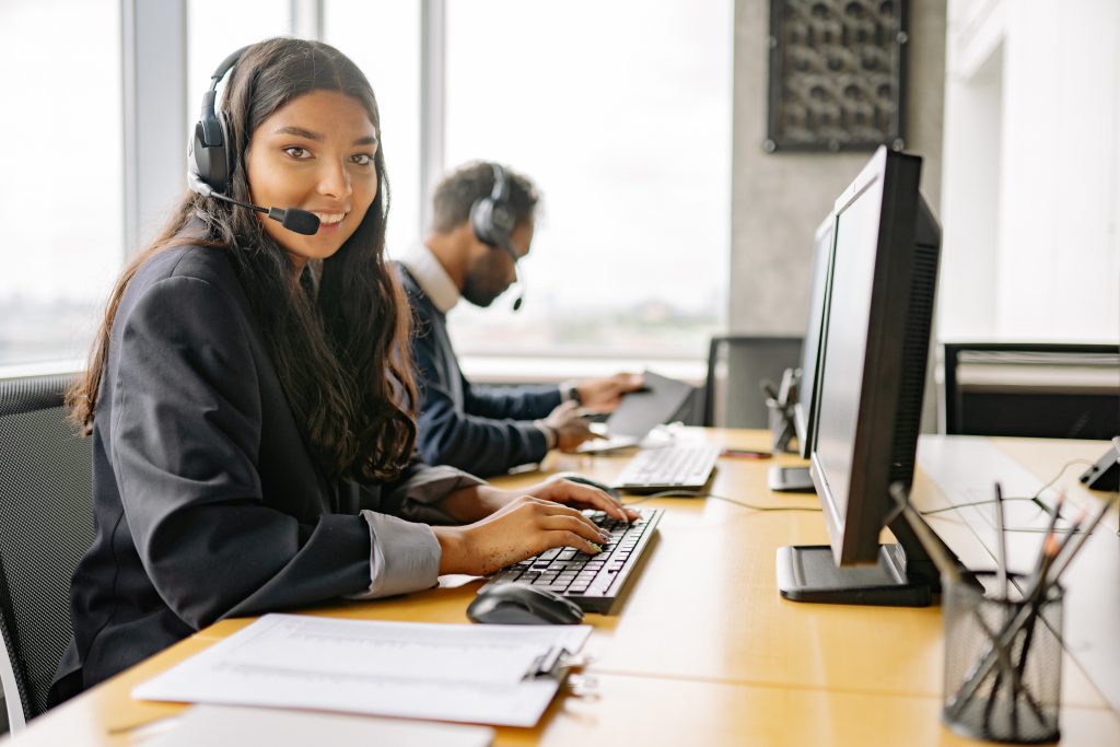 a smiling customer service representative with headphones on her desktop computer